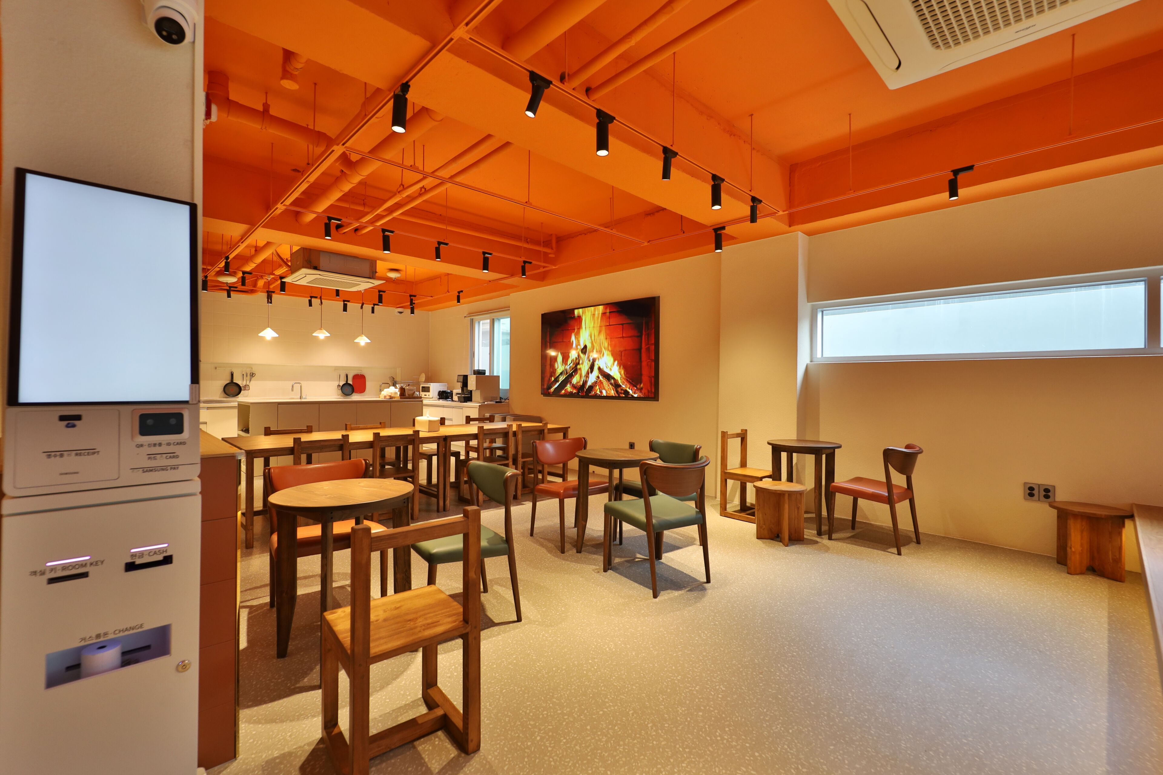 A modern dining area with wooden tables and chairs, a large painting of a fire, and a view of the outside through a window.