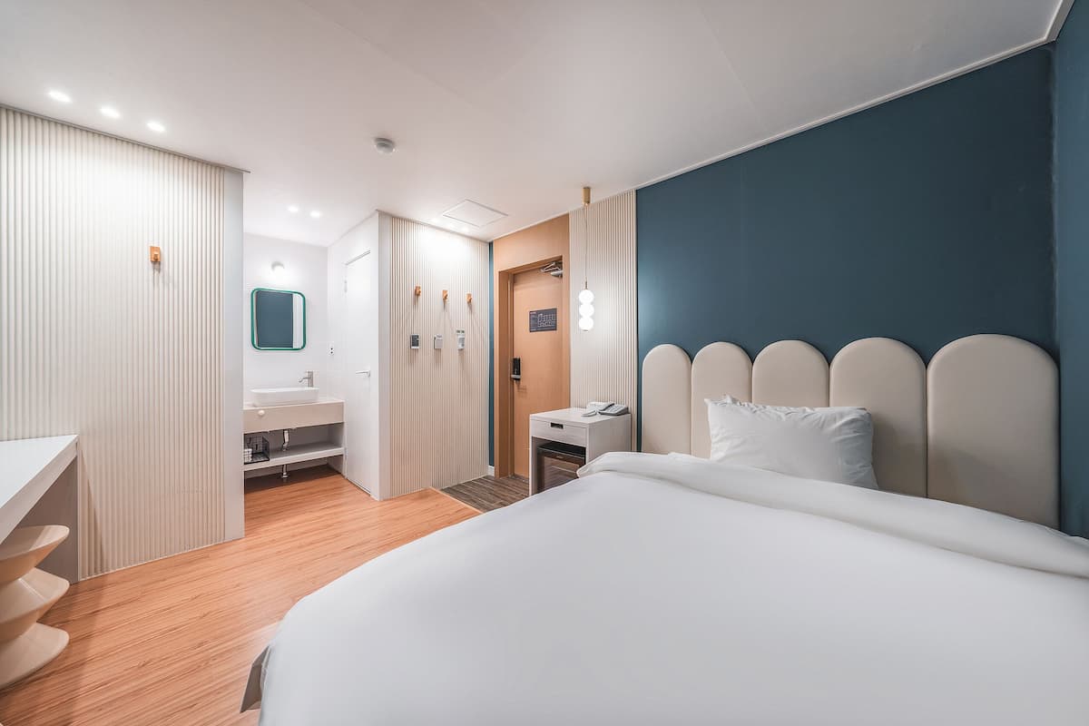 Habitación de hotel moderna con cama, escritorio, baño con lavamanos y espejo, y una pared de acento azul.