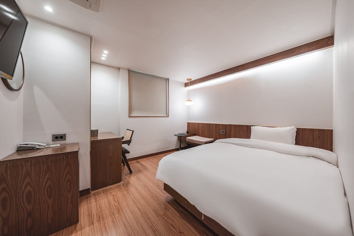 Una habitación de hotel moderna con un escritorio de madera, una cama, una mesita y un espejo.