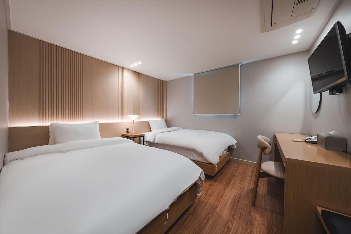 Una habitación de hotel moderna con dos camas, un escritorio, una silla, un televisor y una lámpara de noche.