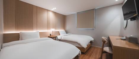 A modern hotel room with two beds, a desk, a chair, a TV, and a bedside lamp.