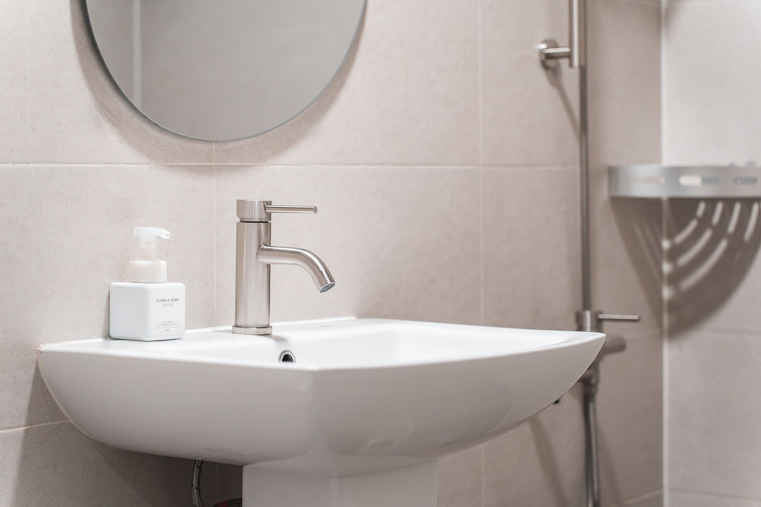 Un baño con un lavabo blanco, un espejo redondo y una zona de ducha.