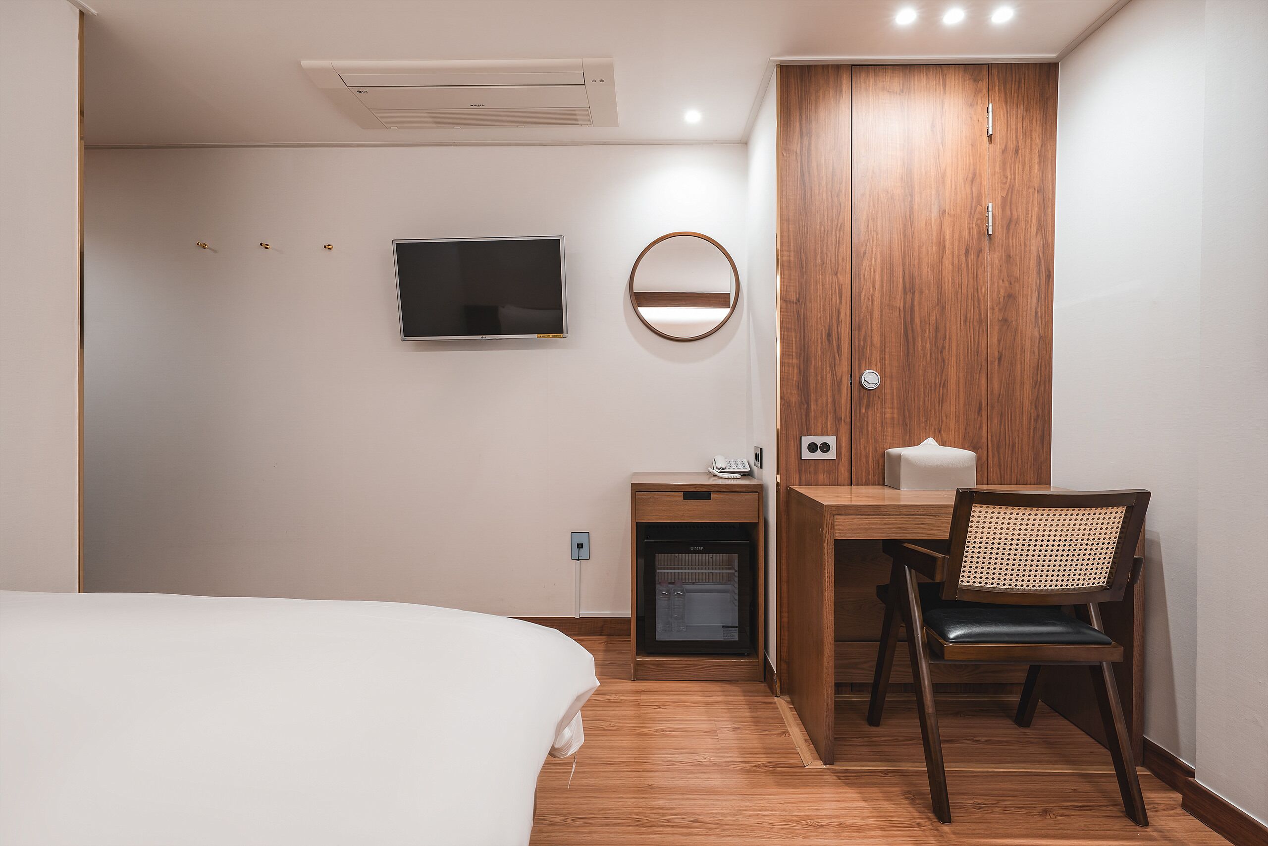 A hotel room with a bed, a desk with a chair, a television, a mirror, and a wardrobe.