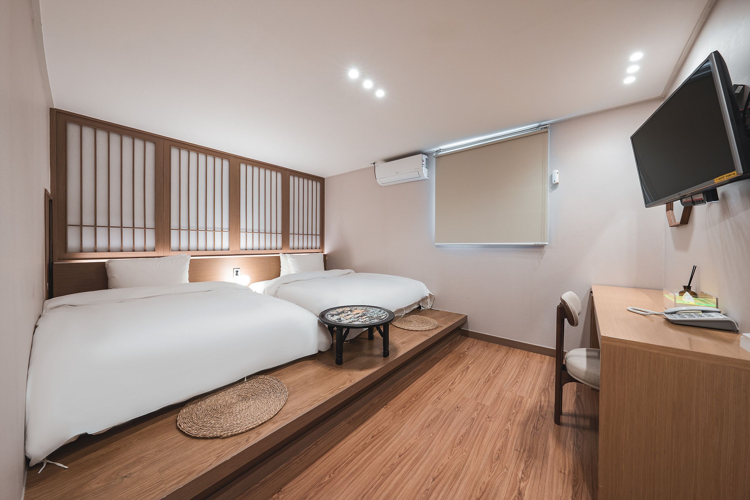 A bedroom with two beds, a desk, a chair, a TV, and an air conditioning unit.