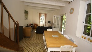 A cozy room with a wooden dining table, white chairs, a sofa, and a television.