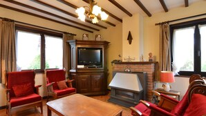 A living room with a fireplace, a television, and two red armchairs.