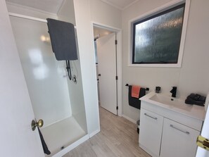 Un baño moderno con cabina de ducha de vidrio, un lavamanos blanco y una toalla negra, y una ventana con vistas.