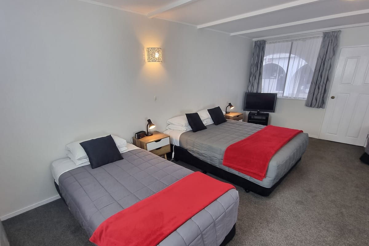 A hotel room with two beds, a TV, a bedside lamp, and a wall-mounted light fixture.