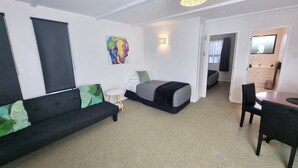 A modern, well-lit room with a bed, a sofa, a small table, and a TV. - Hacienda Motel (Invercargill)