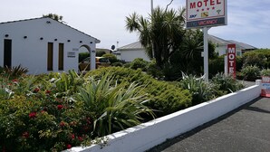 A motel sign with a flag, a guest car area, and a white building with a guest car area sign. - Hacienda Motel (Invercargill)