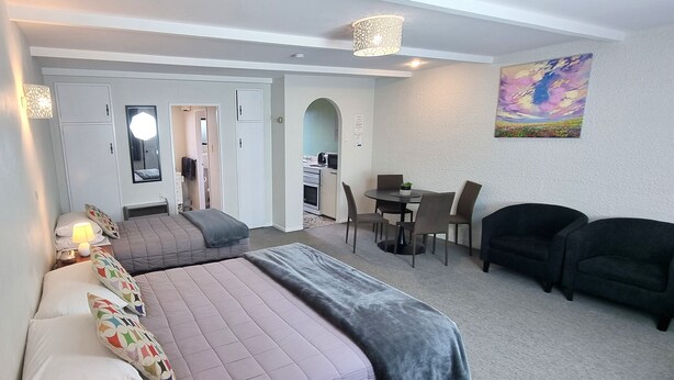 A modern hotel room with two beds, a dining area, and a sofa. - Hacienda Motel (Invercargill)