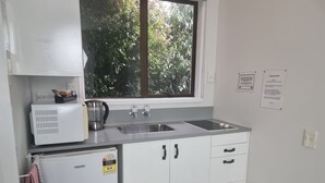 A compact kitchen with a sink, a small refrigerator, and a window with a view of greenery. - Hacienda Motel (Invercargill)