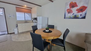 A compact kitchen with white appliances, a dining table with four chairs, and a painting of red flowers on the wall. - Hacienda Motel (Invercargill)