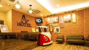 A hotel reception area with a brick wall, a vintage car, and green upholstered seating. - A Plus Boutique Hotel (Sekinchan)