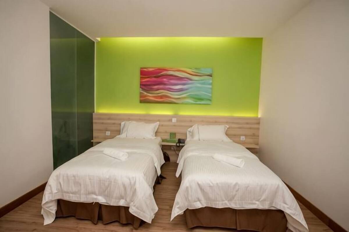 Una habitación de hotel con dos camas, una pared verde y un cuadro abstracto colorido.
