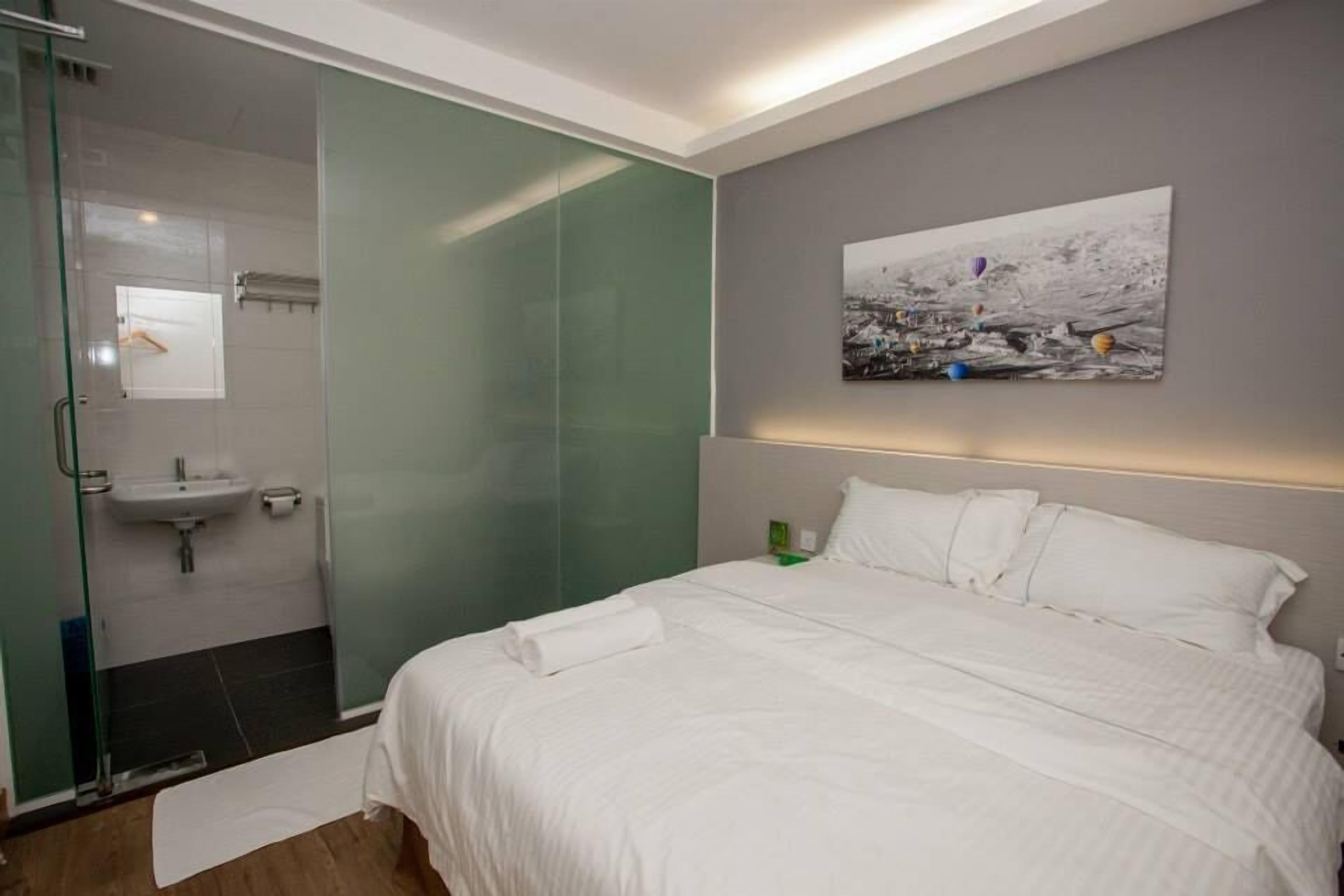 Una habitación de hotel moderna con ducha envuelta en vidrio, una cama blanca y un cuadro en la pared.