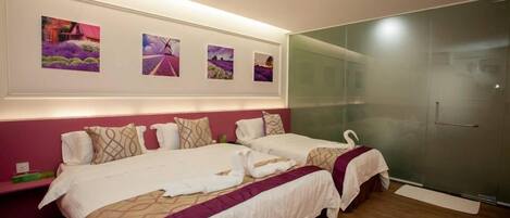 Habitación de hotel con dos camas, un separador de vidrio y obras de arte en la pared.