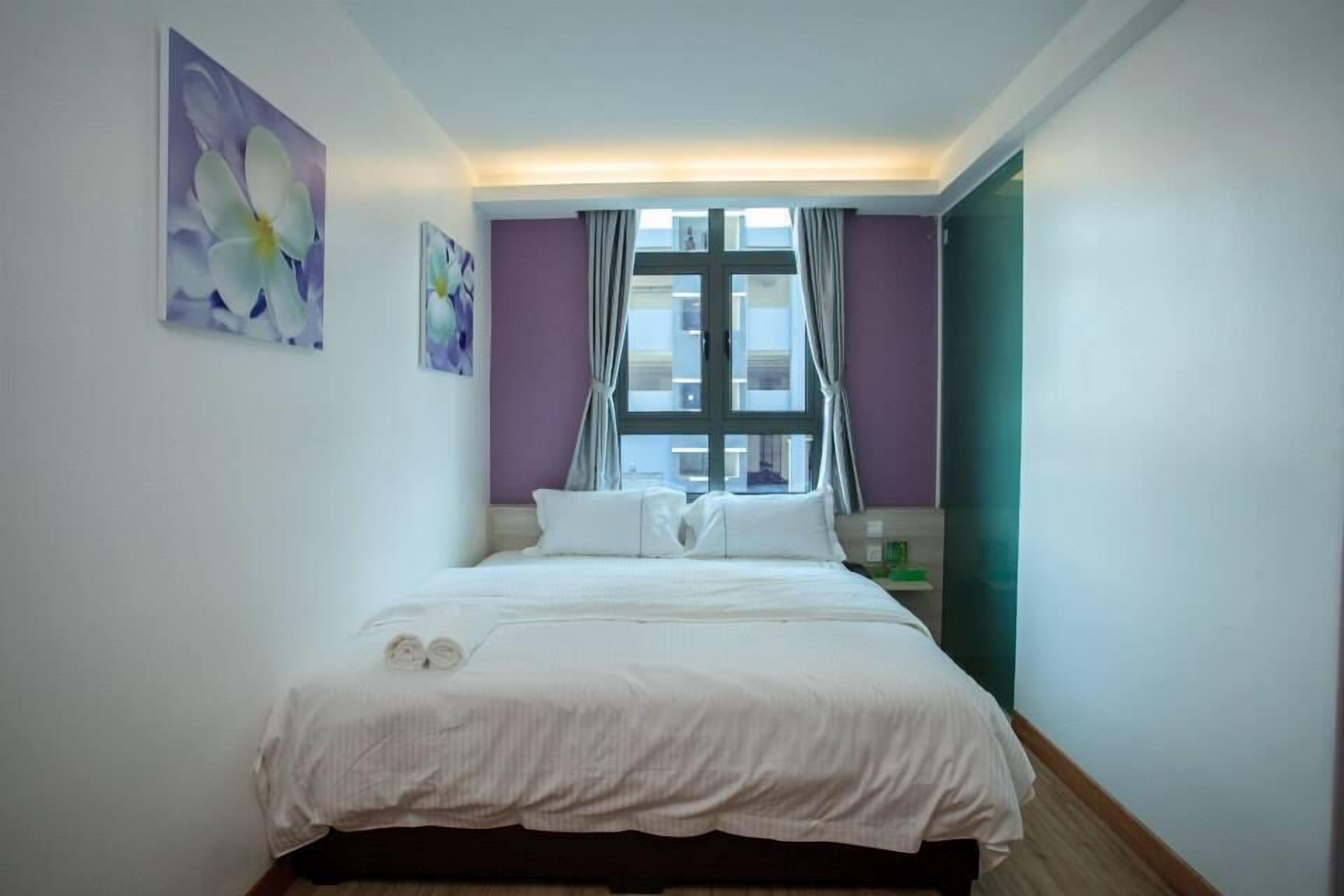 A neatly made bed with white linens, a window with curtains, and two wall-mounted paintings.
