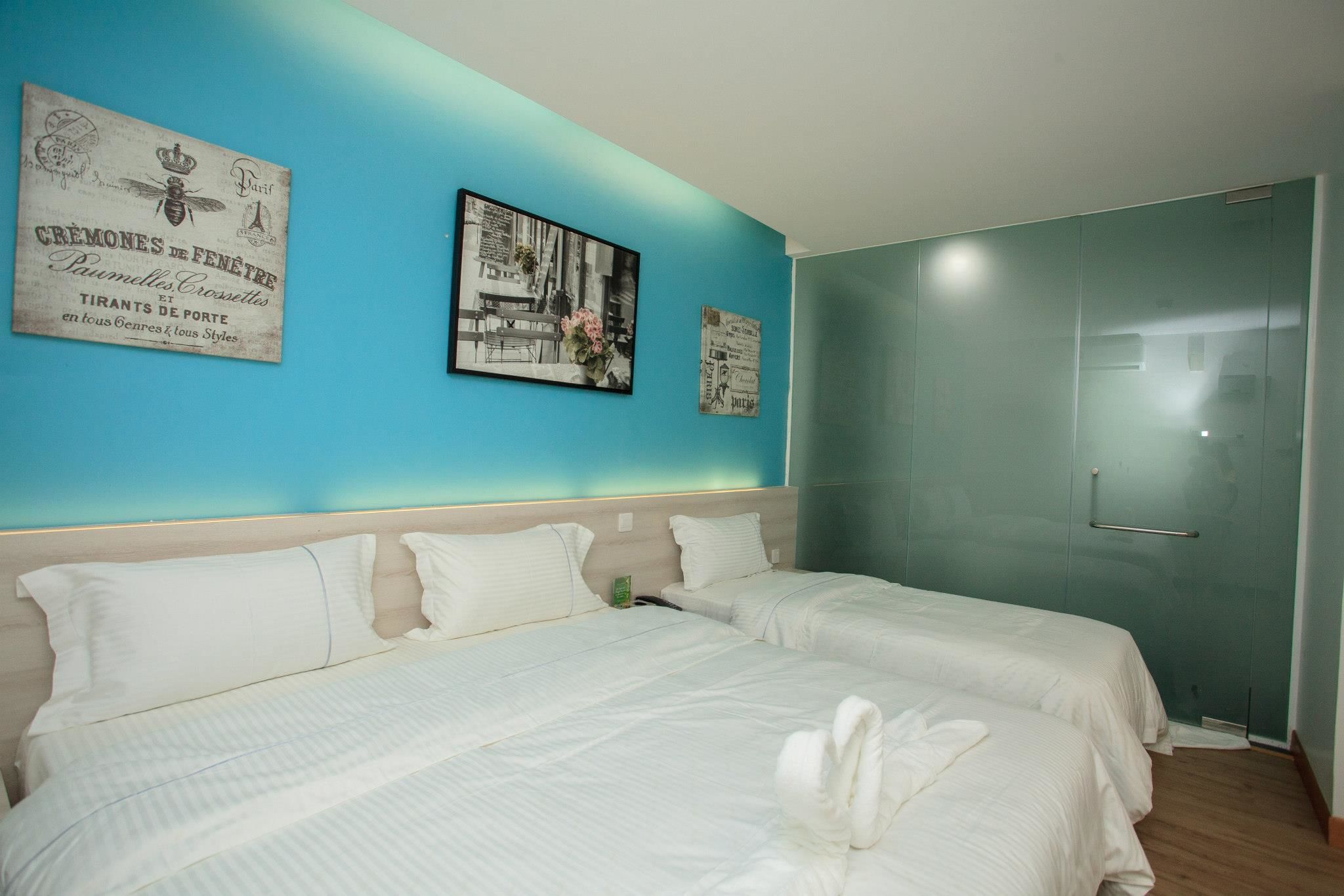 A hotel room with two beds, a teal accent wall, and a framed picture of a cityscape.