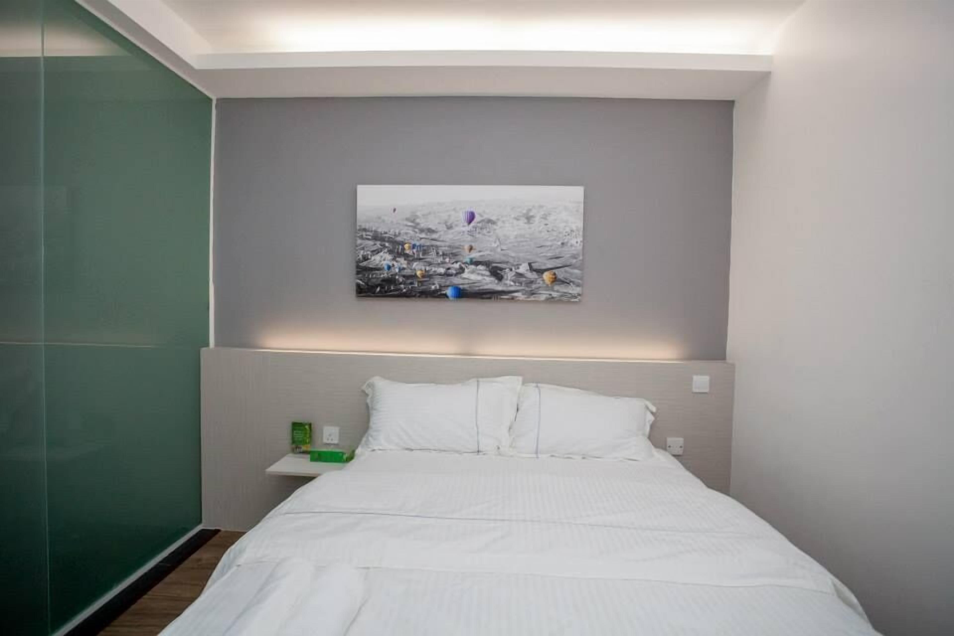 A hotel room with a bed, a nightstand, a green wall, and a painting of hot air balloons.