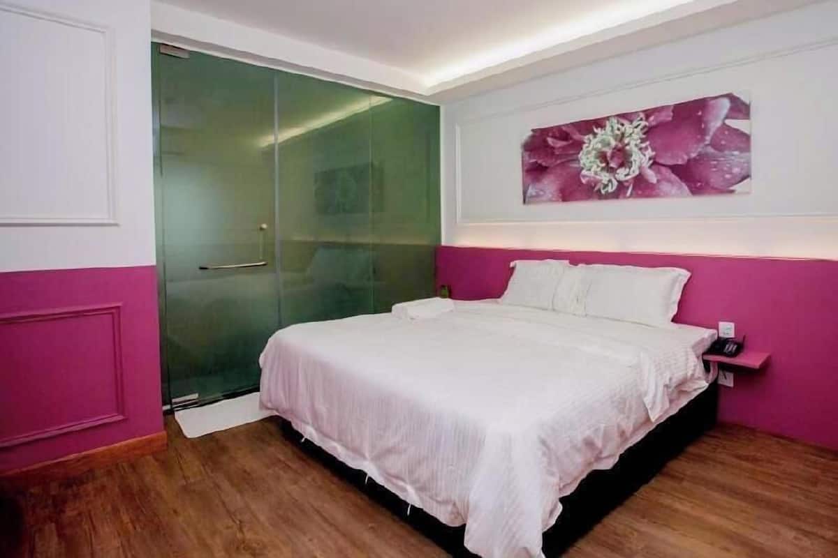 Un dormitorio con mampara de vidrio en la ducha, cama con ropa de cama blanca y una pared de acento en color rosa.