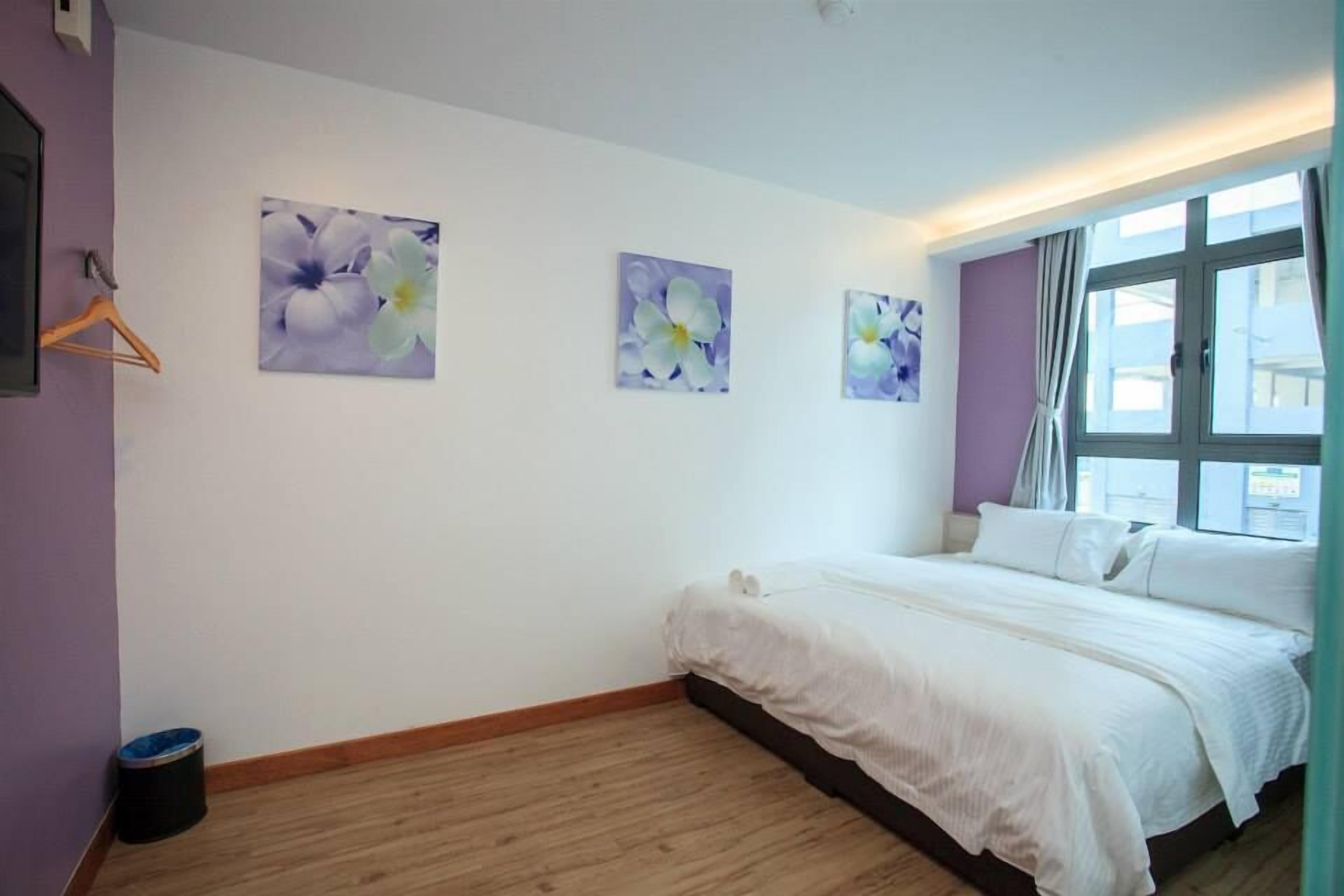 A bedroom with a large bed, a window with curtains, and three wall-mounted flower paintings.