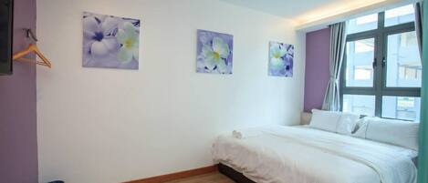 A bedroom with a large bed, a window with curtains, and three wall-mounted flower paintings.
