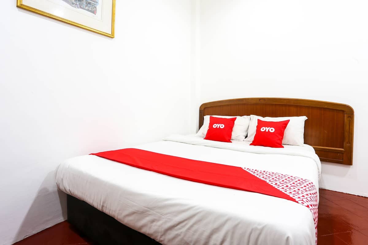 Una cama bien hecha con ropa de cama blanca y roja, un cabecero de madera y un cuadro en la pared.