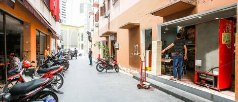 Una calle estrecha con motocicletas estacionadas y una persona parada frente a la entrada de una tienda.
