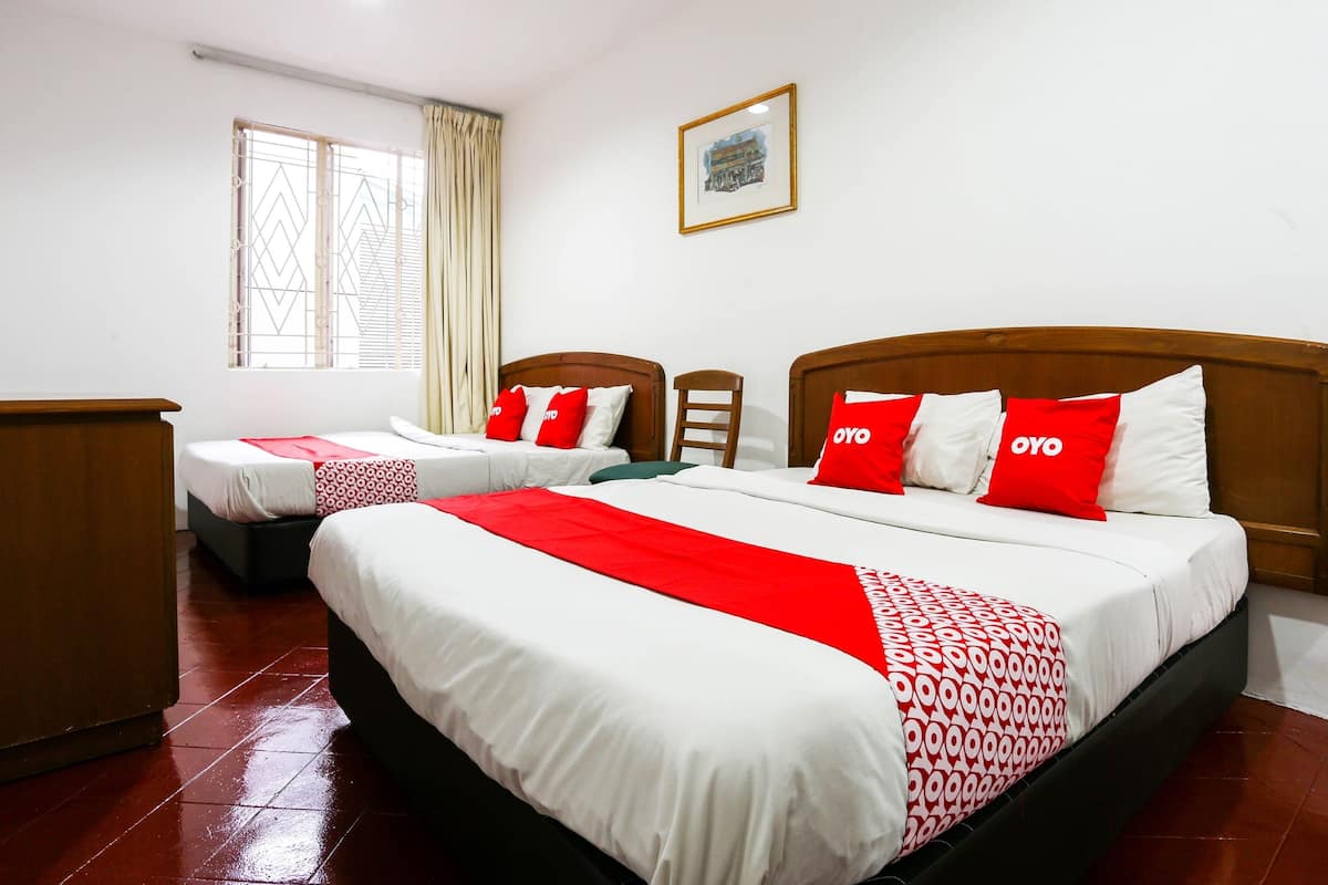 Habitación de hotel con dos camas, cada una con ropa de cama roja y blanca, un cabecero de madera y una ventana con cortinas.
