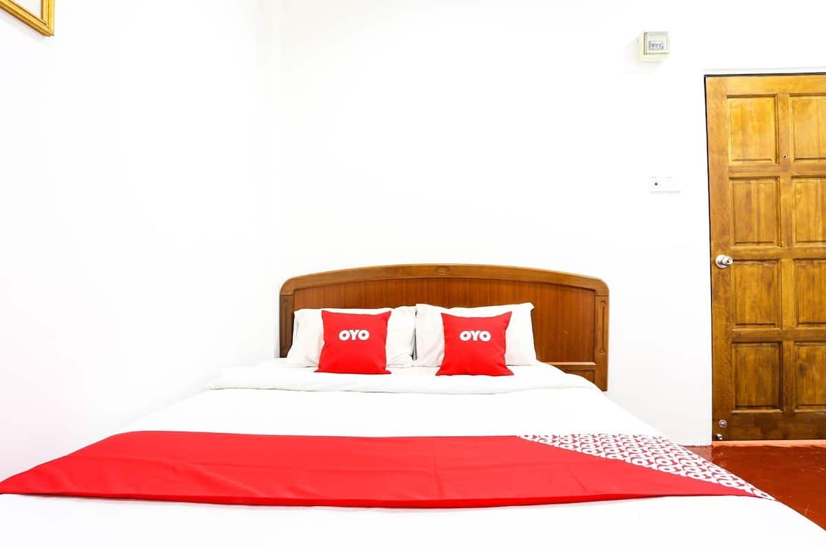 Una cama con cabecera de madera, dos almohadas rojas con el texto 'OYO', ropa de cama blanca y una manta roja.