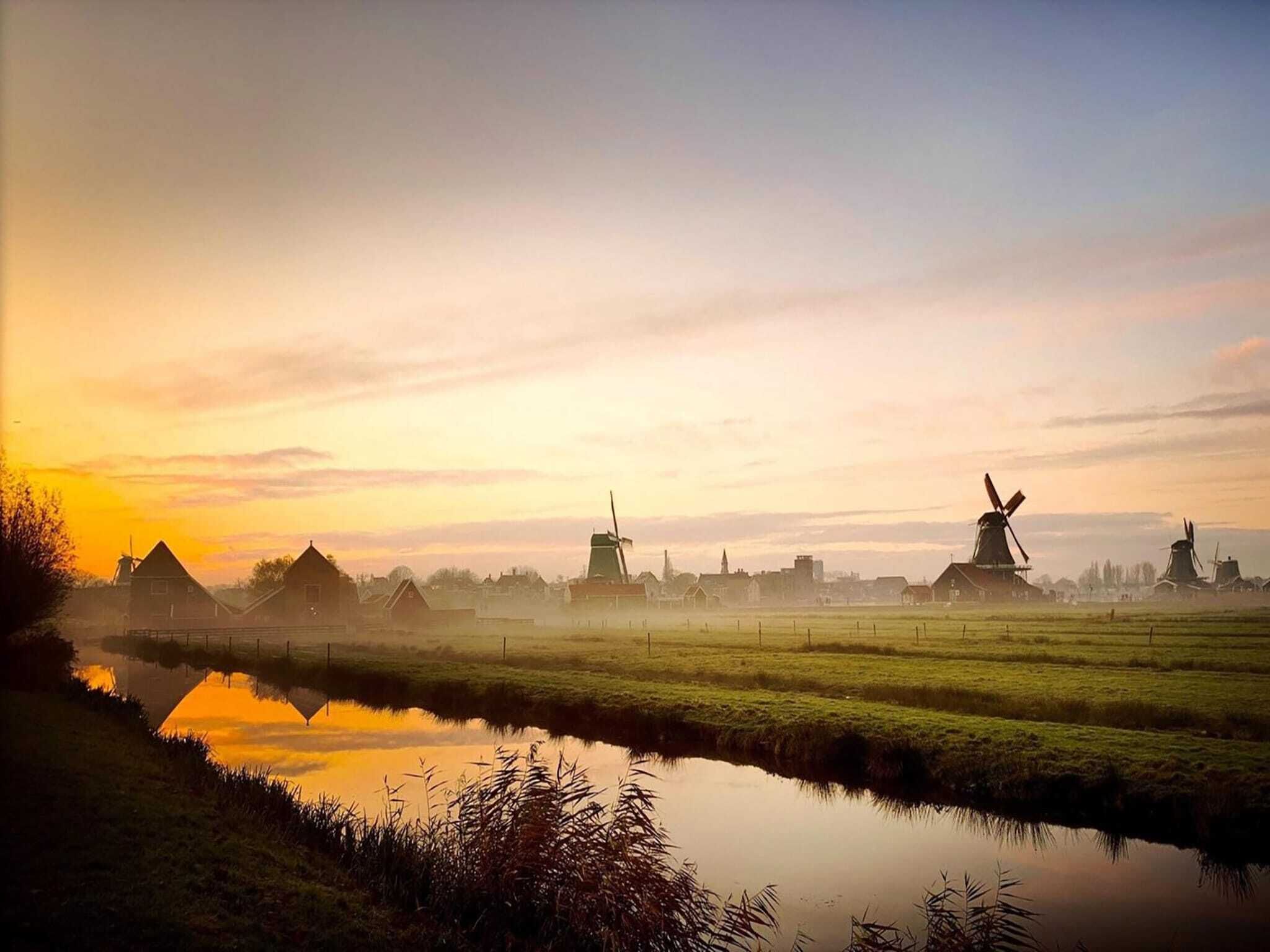 A serene landscape with windmills and a calm river reflecting the sky.