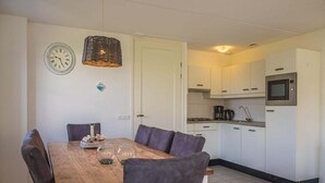Kompakti keittiö, jossa on valkoiset kaapit, mikroaaltouuni sekä ruokailutila, jossa on puinen pöytä ja harmaat tuolit.