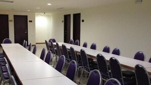 Una sala de conferències amb taules llargues i cadires, equipada amb llums al sostre i ventilació.