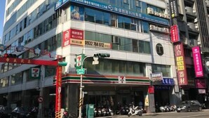 Un edifici de diverses plantes amb diferents comerços a la planta baixa, com un 7-Eleven i un hotel.