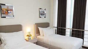 Habitación de hotel con dos camas, una mesita de noche con una lámpara y un jarrón de flores, y dos cuadros en la pared.