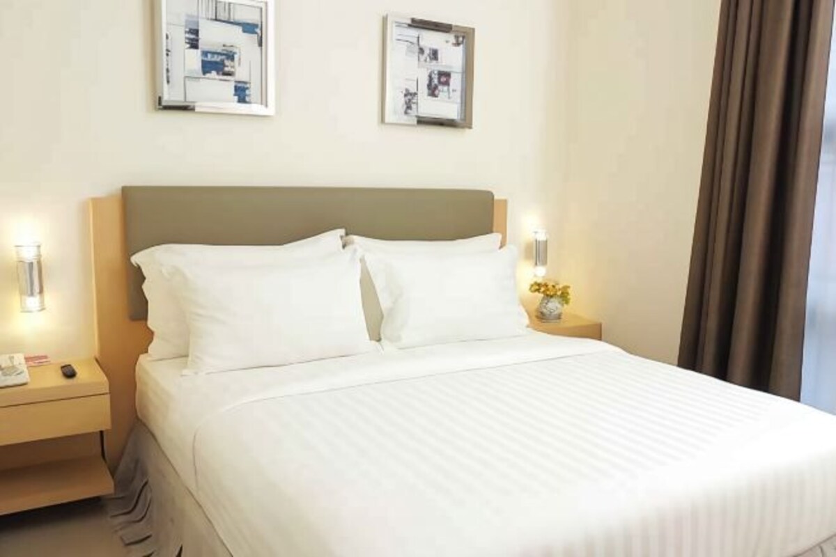 Una cama bien hecha con sábanas blancas, un cabecero de madera y dos mesitas de noche con lámparas.