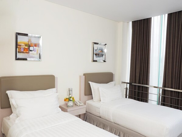 Ein Hotelzimmer mit zwei Betten, einem Nachttisch mit Telefon und einer Blumenvase, sowie zwei gerahmten Bildern an der Wand.
