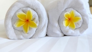 Dos toallas blancas enrolladas cuidadosamente con motivos florales amarillos sobre una cama.