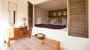 Una camera da letto con una cassettiera in legno, un comodino, una finestra con persiane e un letto con cuscini.