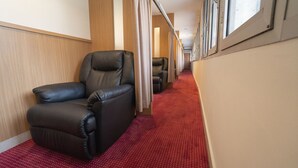 A narrow corridor with red carpet flooring, wooden panel walls, and leather seating areas.