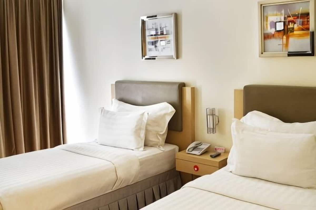 A hotel room with two beds, a nightstand with a phone, and a wall-mounted picture.