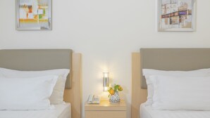A hotel room with two beds, a bedside table with a lamp, a vase with flowers, and two framed pictures on the wall.