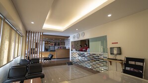 A hotel reception area with a counter, a seating area with chairs, a reception desk, and a wall with clocks and a sign indicating the internet corner.
