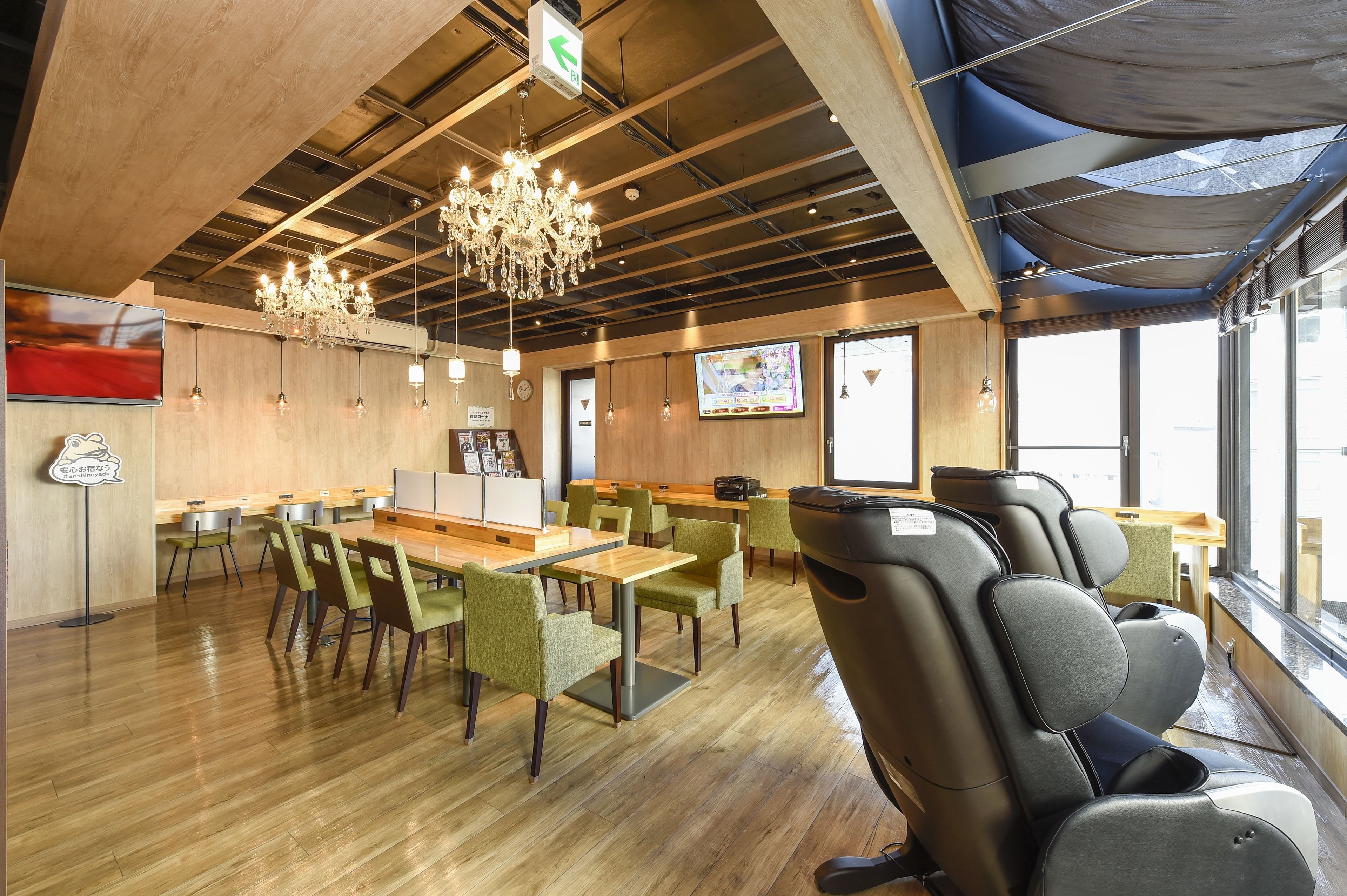 A modern dining area with wooden floors, green upholstered chairs, and a chandelier.