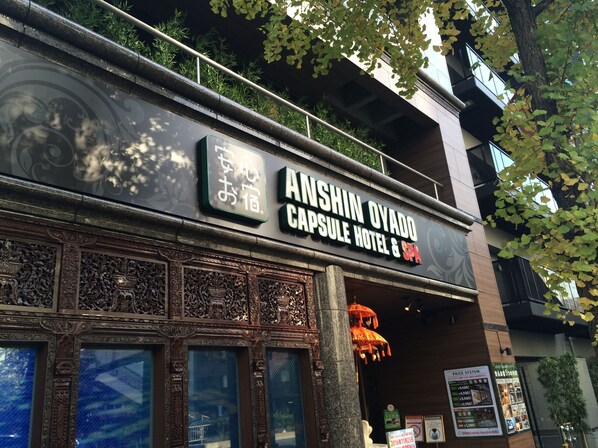 The exterior of Anshin Oyado Capsule Hotel & Spa, featuring a traditional architectural design with intricate carvings and a modern facade.