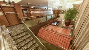 Un hall d’hôtel avec un escalier central, un distributeur automatique et une plante décorative.