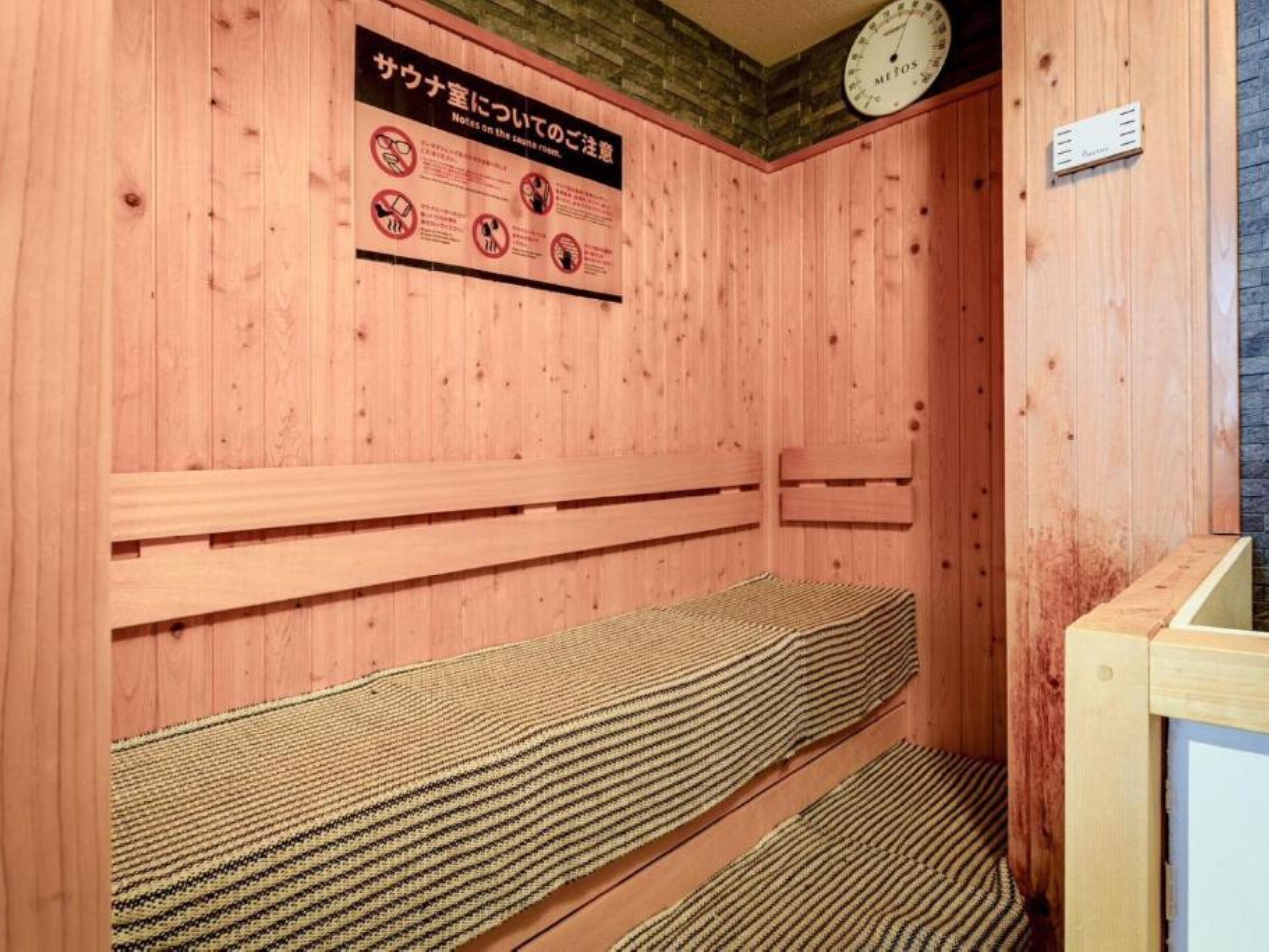 A sauna room with wooden walls, a bench, a clock, and a sign with instructions.