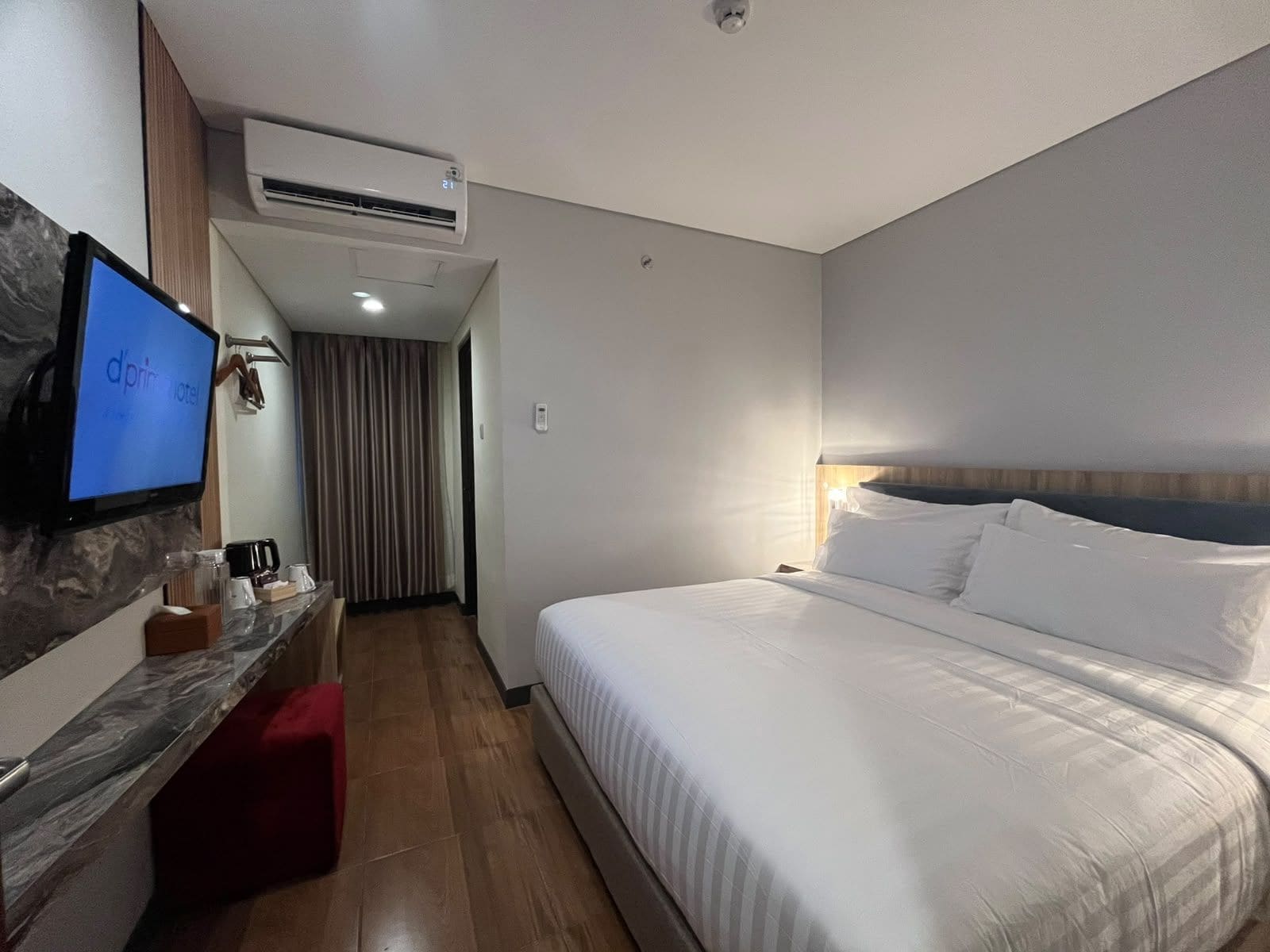 A hotel room with a bed, a TV, a coffee station, and an air conditioning unit.