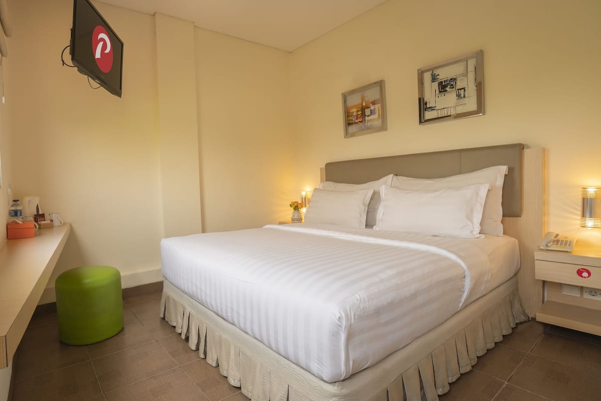 A neatly arranged hotel room with a bed, bedside table, and a green stool.